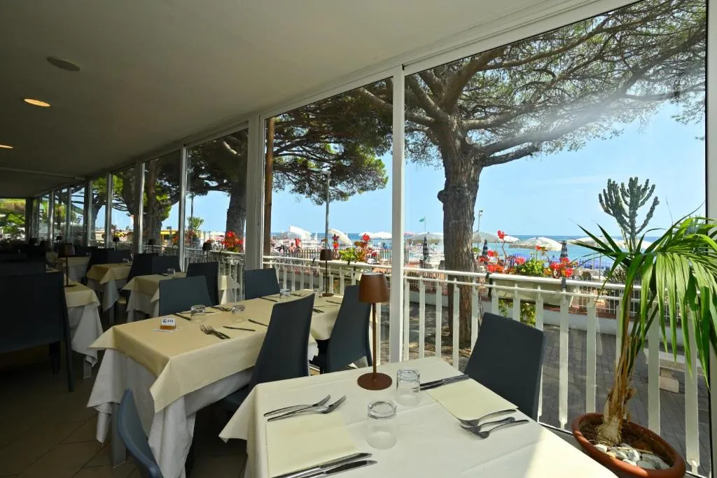 Sala ristorante con tavoli apparecchiati e ampie vetrate con vista sulla spiaggia