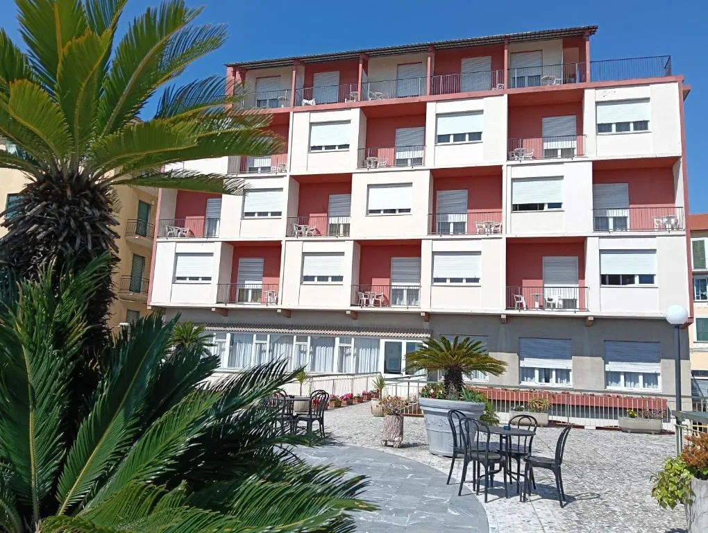 Facciata esterna dell'hotel con balconi e terrazza con tavoli e palme