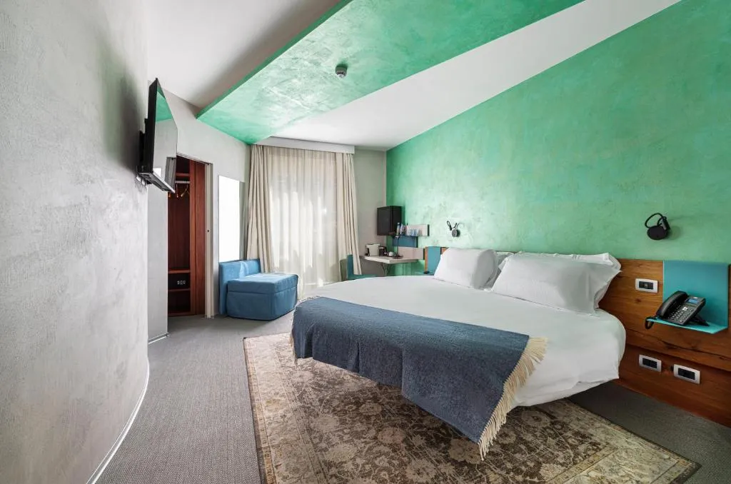 Camera matrimoniale con parete e soffitto verdi, letto, poltrona blu e tappeto decorato