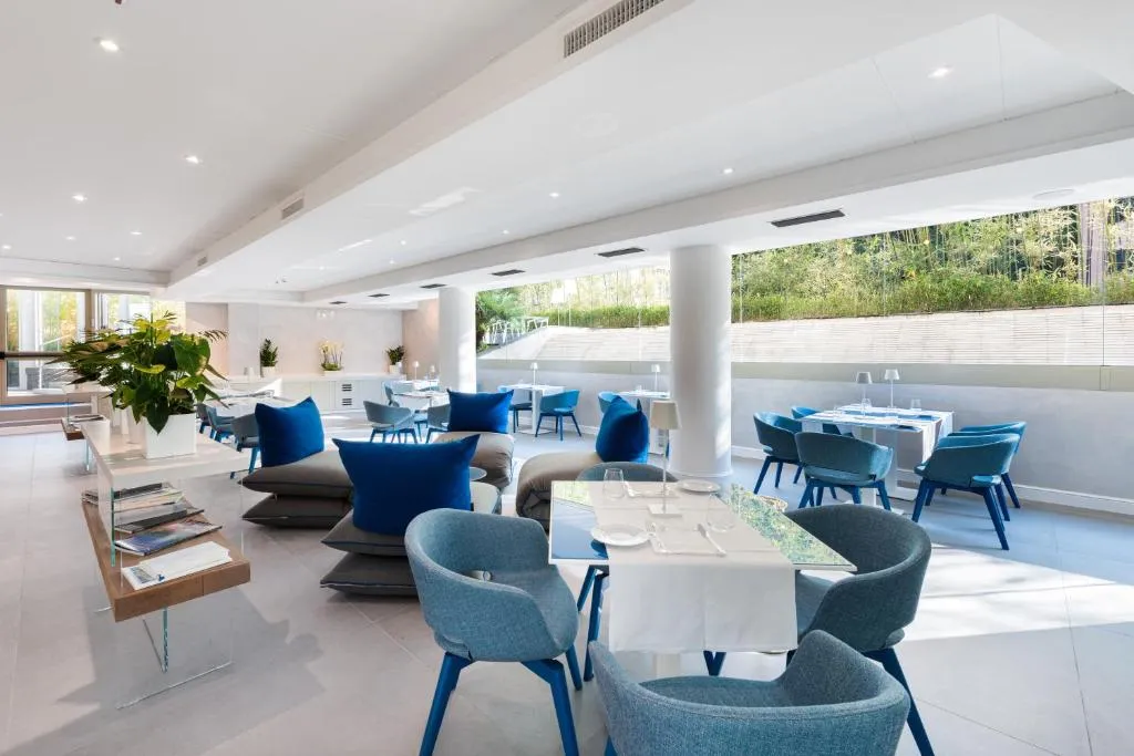 Sala ristorante luminosa con tavoli, sedie e poltrone blu affacciata sul verde