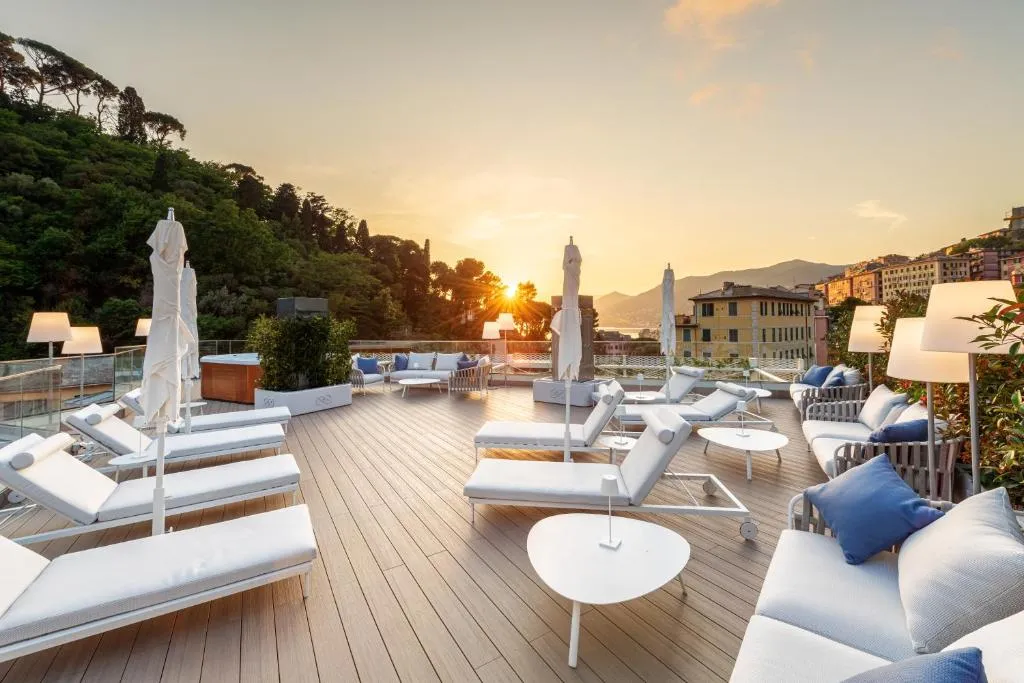 Terrazza solarium al tramonto con lettini bianchi, divani e vista sulle colline e sul mare