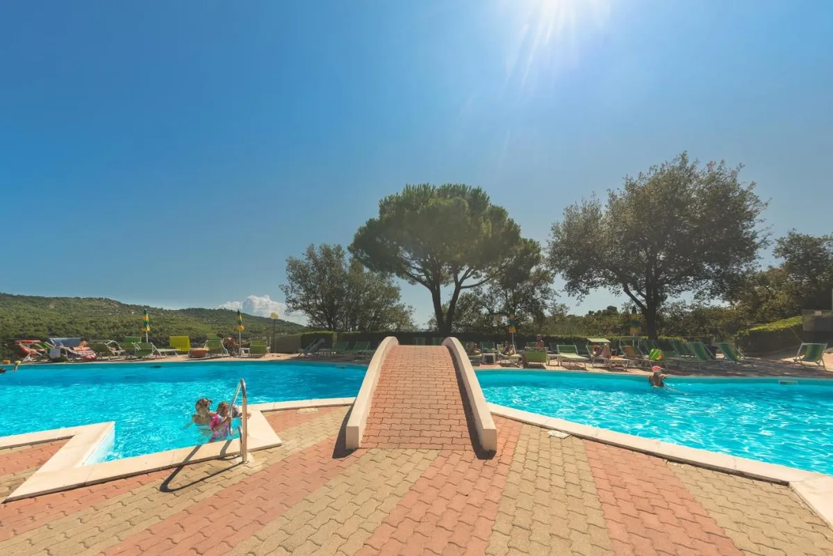 Piscina con pontile centrale e lettini, alberi e colline sullo sfondo