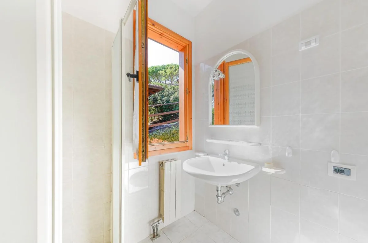 Bagno bianco con doccia, lavabo e finestra con vista sul verde