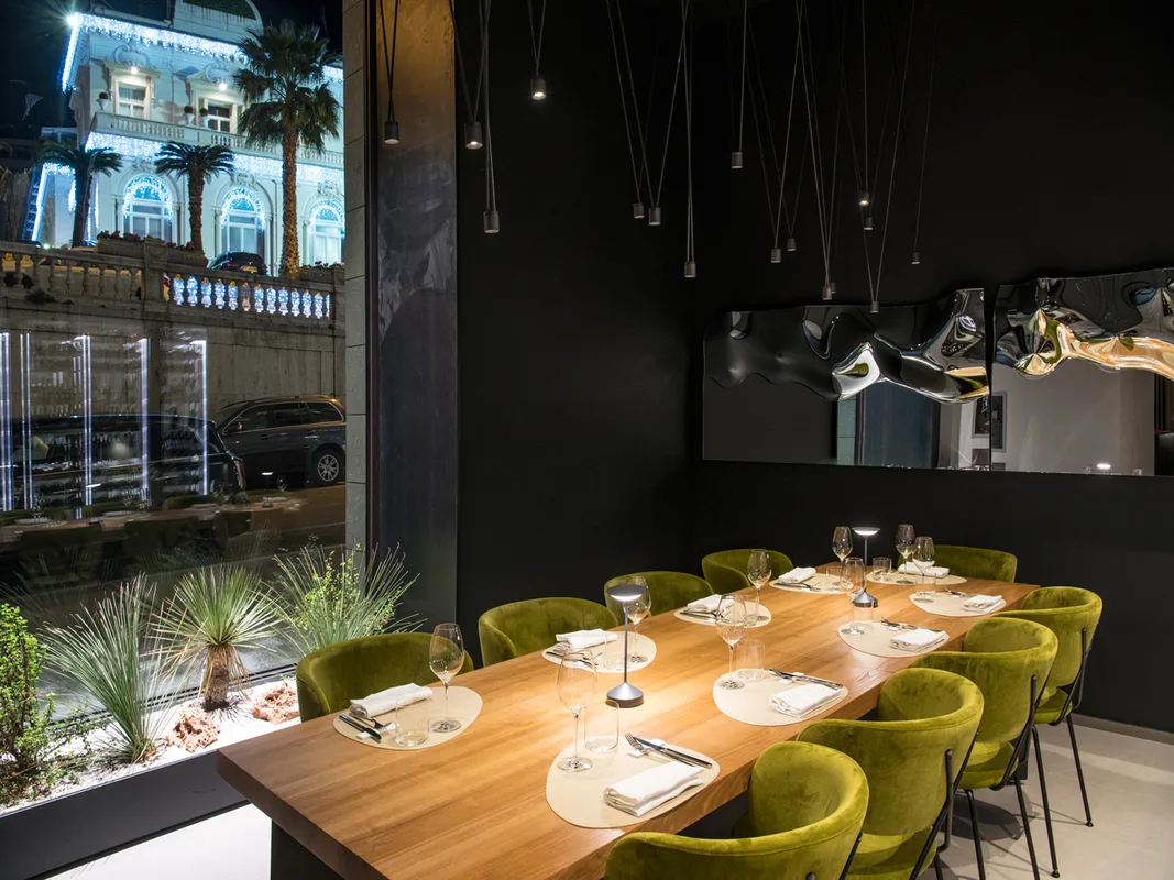 Sala da pranzo elegante con tavolo in legno, sedie verdi e vista sulla strada illuminata
