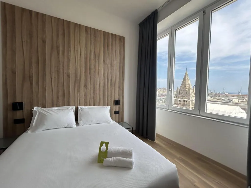 Camera moderna con testiera in legno e ampie finestre con vista sulla Lanterna di Genova