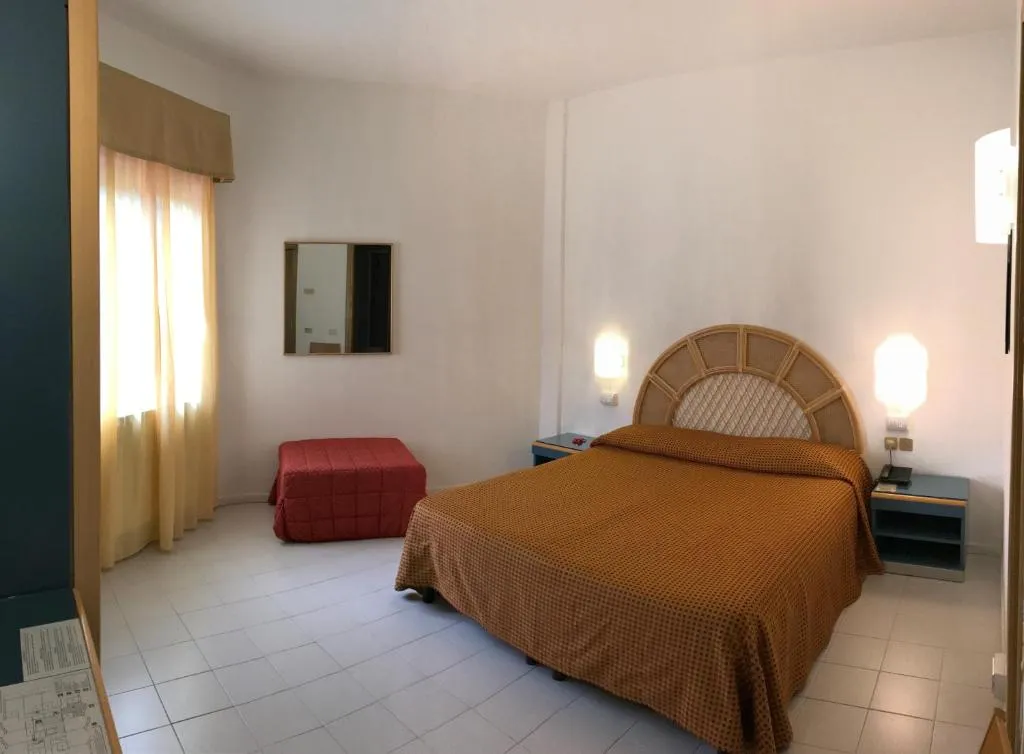 Camera matrimoniale con copriletto arancione, pouf rosso e tende gialle