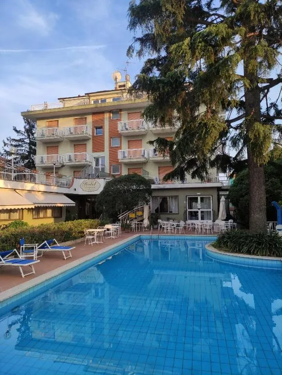 Esterno dell'hotel con piscina, lettini e grande albero ombreggiante