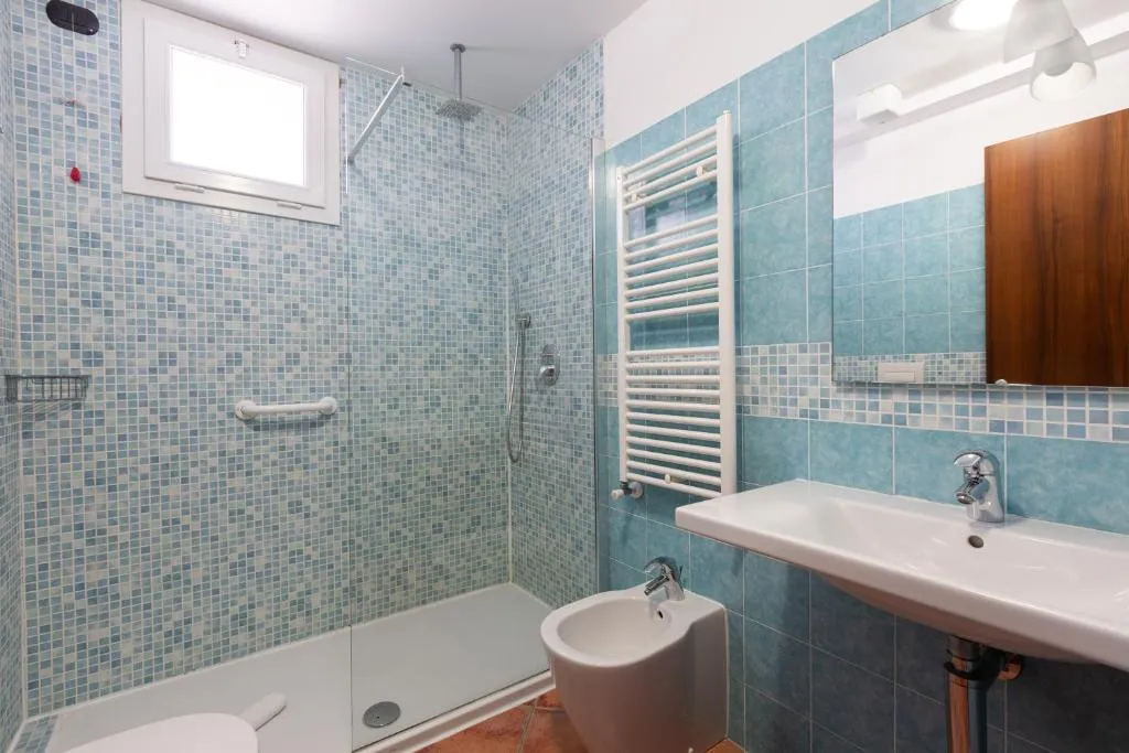 Bagno con doccia, mosaico azzurro, bidet, lavabo e scaldasalviette