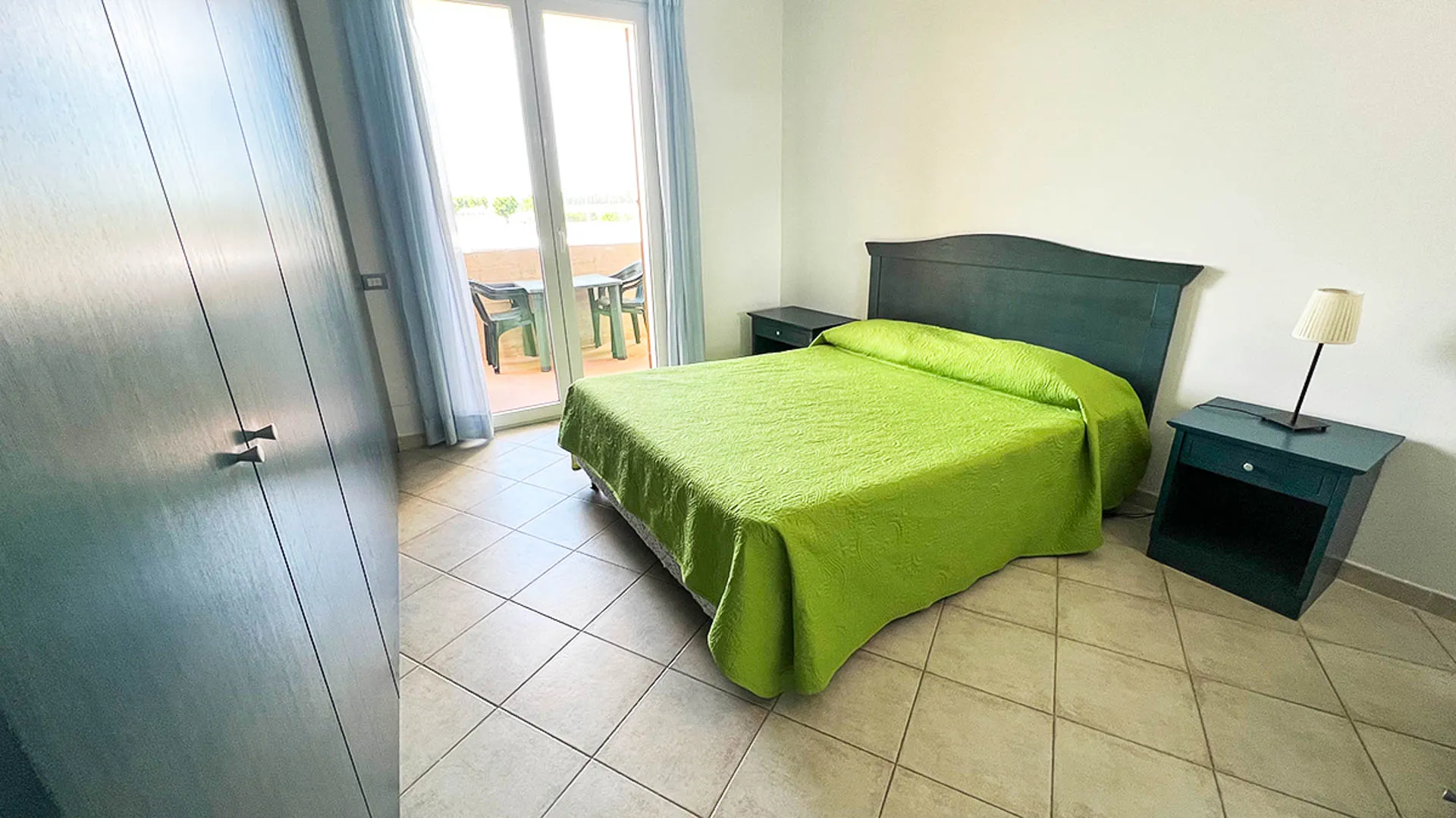 Camera da letto con copriletto verde e accesso al balcone