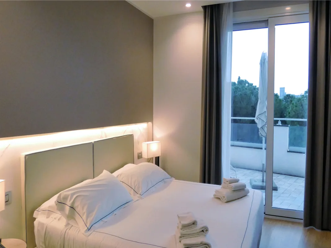 Camera matrimoniale con testiera illuminata e uscita su terrazza con ombrellone