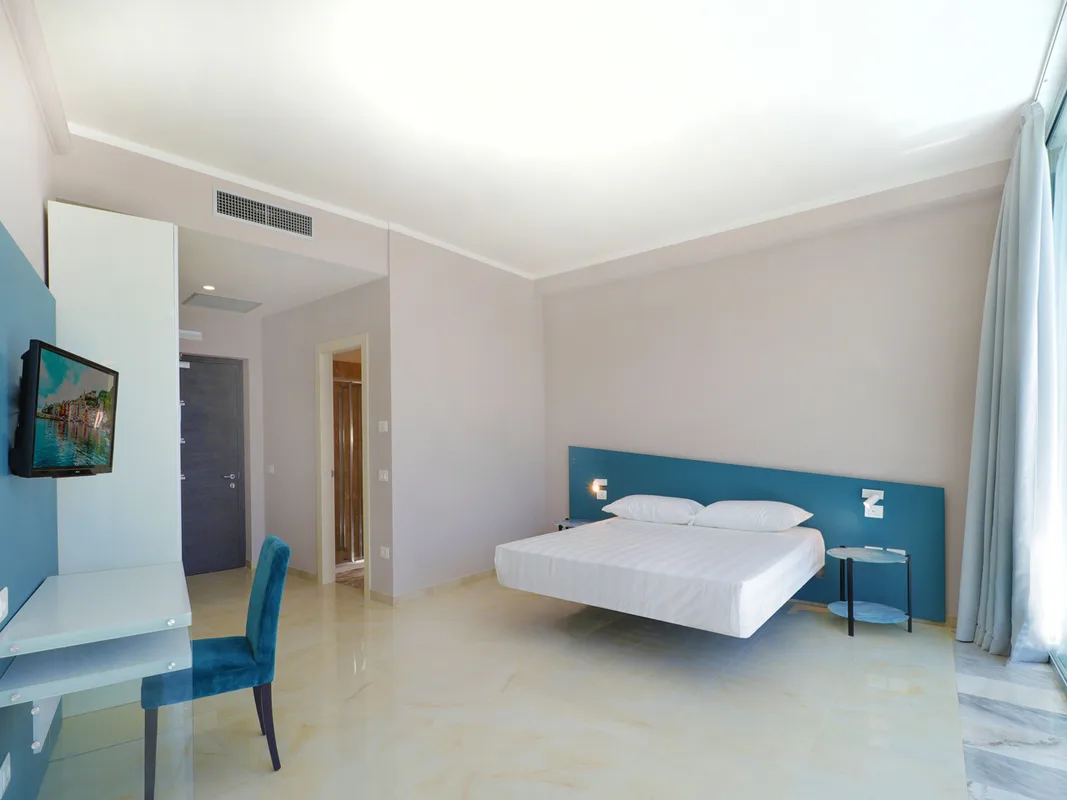 Ampia camera minimalista con letto sospeso, testiera blu, scrivania in vetro e TV