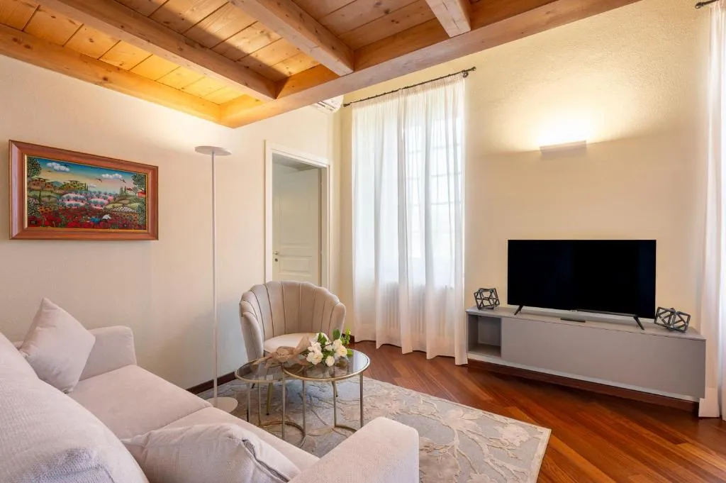 Salotto luminoso con soffitto in travi di legno, divano chiaro, TV e quadro colorato