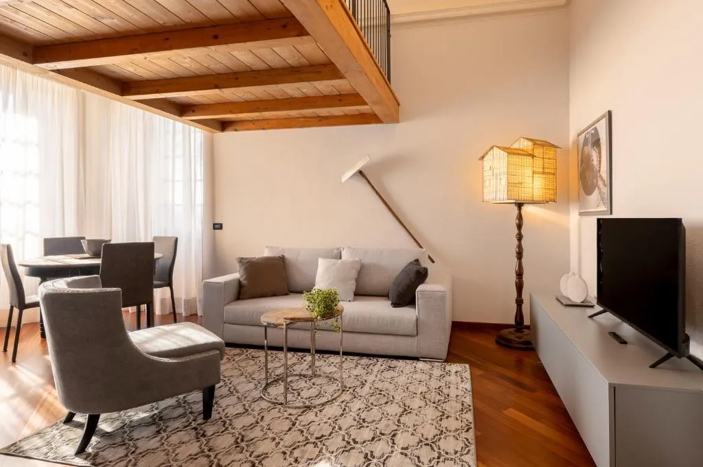 Soggiorno con soffitto in travi di legno, divano bianco, poltrona grigia e zona TV