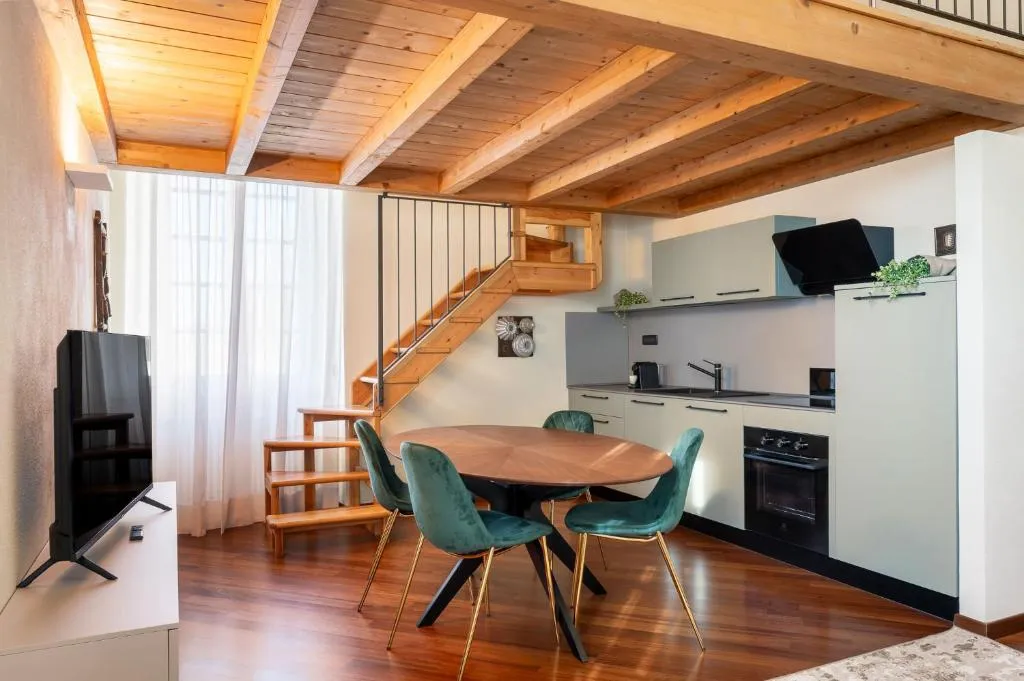 Open space con cucina, tavolo da pranzo con sedie verdi e scala in legno verso il soppalco