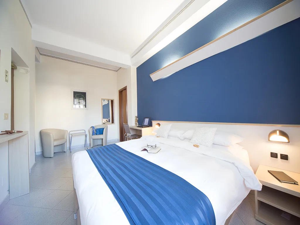 Camera doppia moderna con parete blu, letto matrimoniale e zona salotto