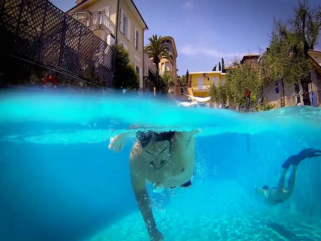 Persone che nuotano in piscina con vista subacquea e edifici dell'hotel sullo sfondo
