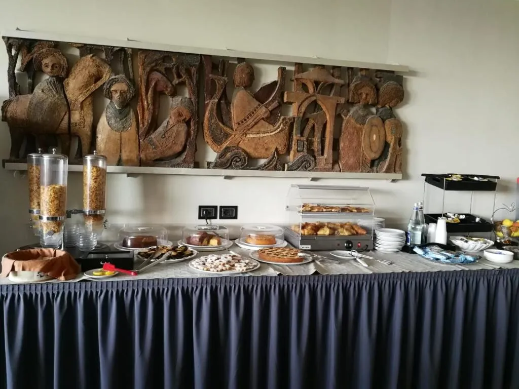 Buffet della colazione con torte, crostate e dispenser di cereali sotto bassorilievo in legno