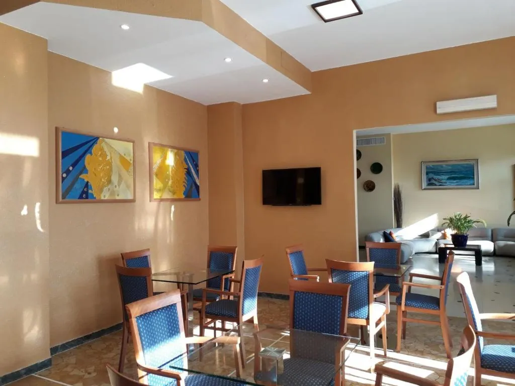 Sala comune con tavoli in vetro, sedie blu, TV a parete e dipinti colorati