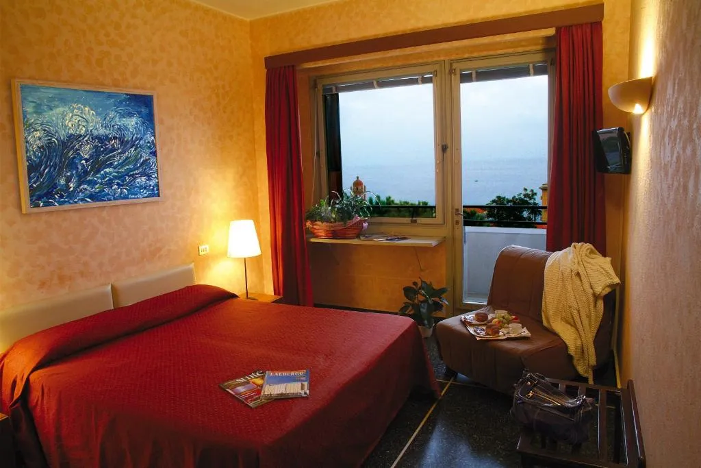 Camera matrimoniale con copriletto rosso, poltrona letto e finestra con vista mare