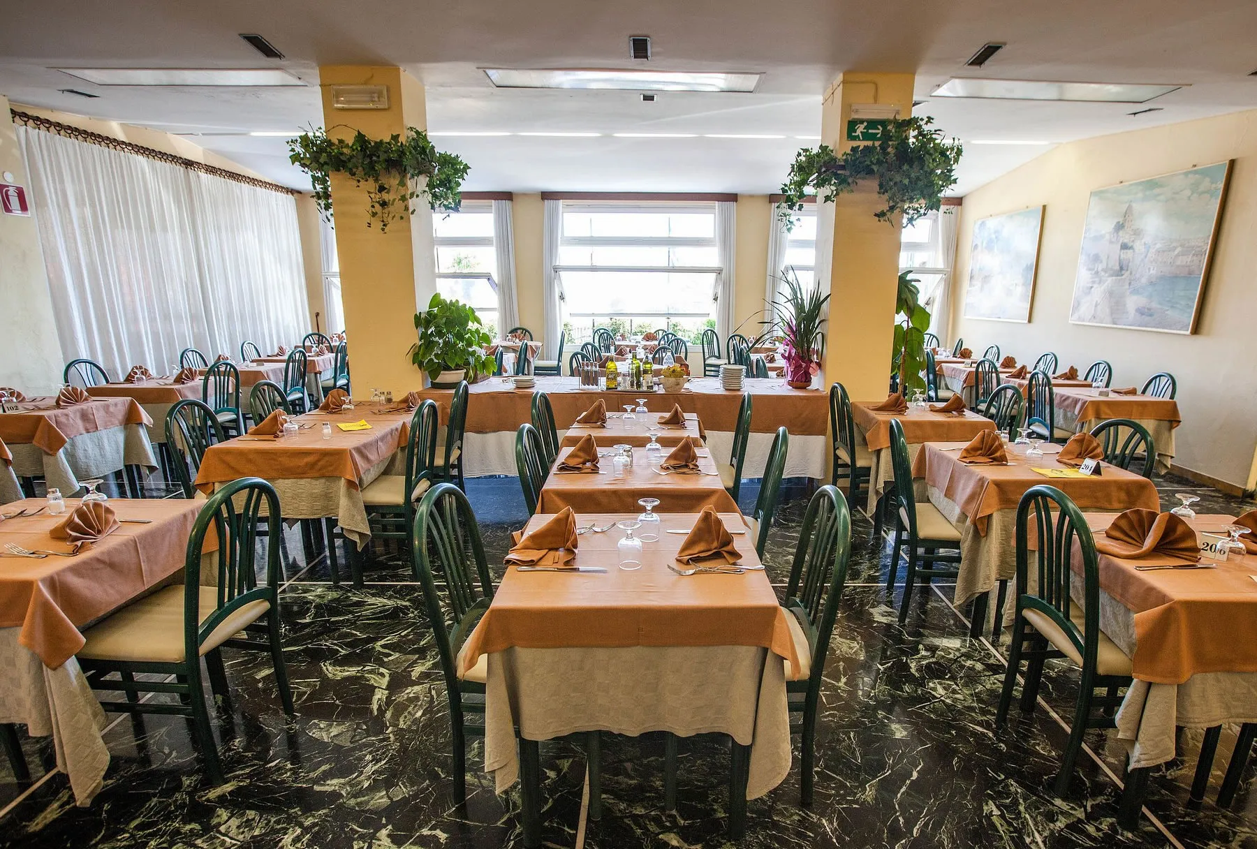 Ampia sala ristorante con tavoli apparecchiati con tovaglie arancioni e sedie verdi