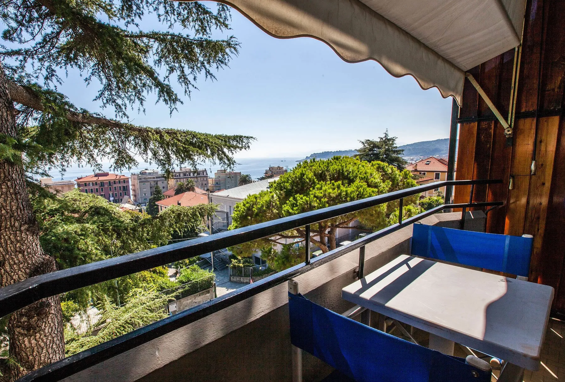 Balcone con tavolino e sedie blu affacciato sulla costa e sul mare tra la vegetazione