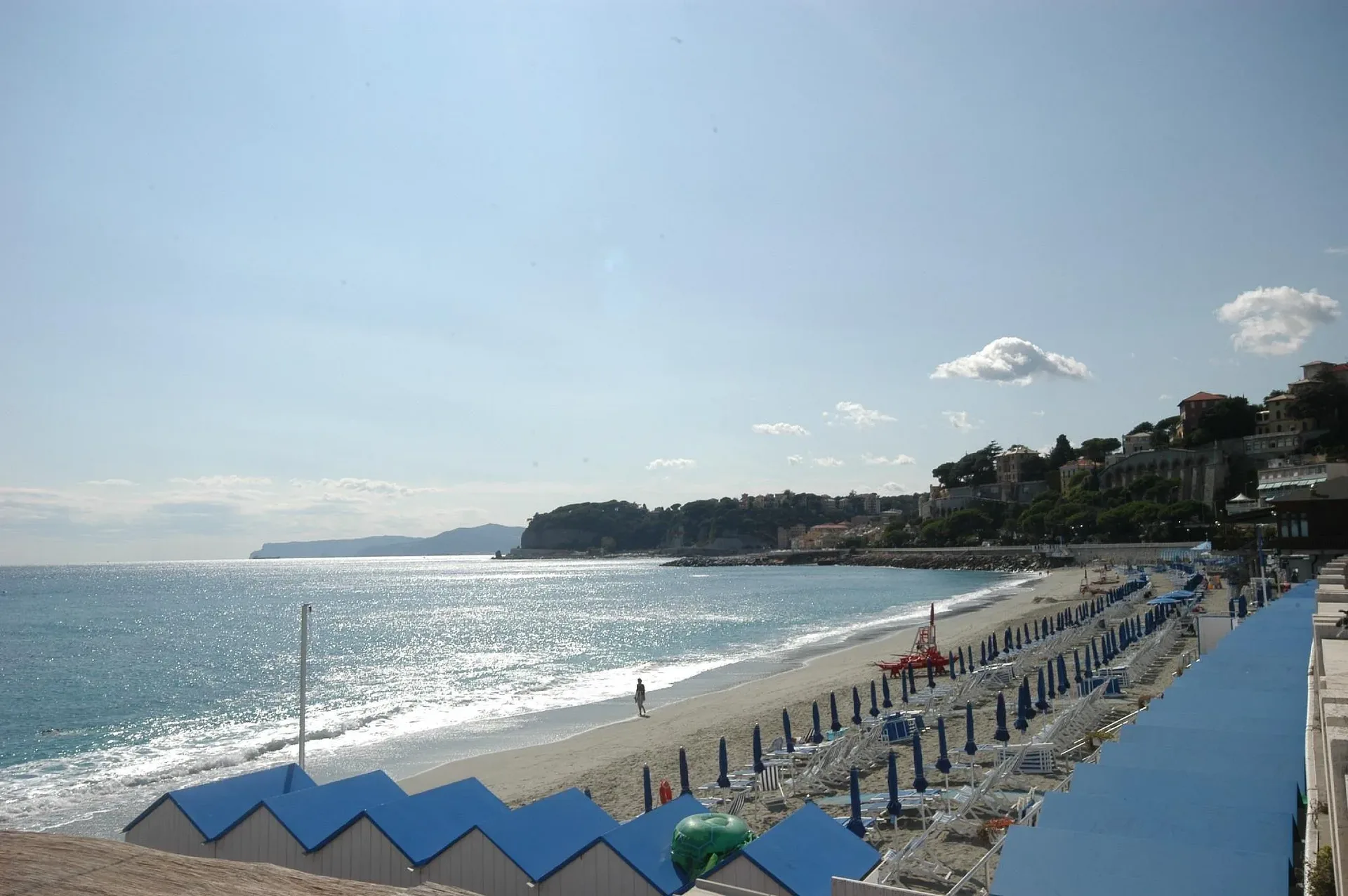 Spiaggia di sabbia con ombrelloni blu, lettini e cabine vista sul promontorio
