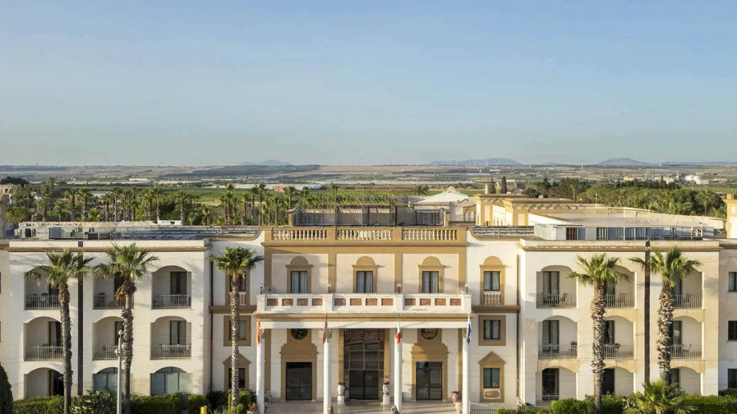 Facciata principale dell'hotel circondata da palme con vista sulla campagna