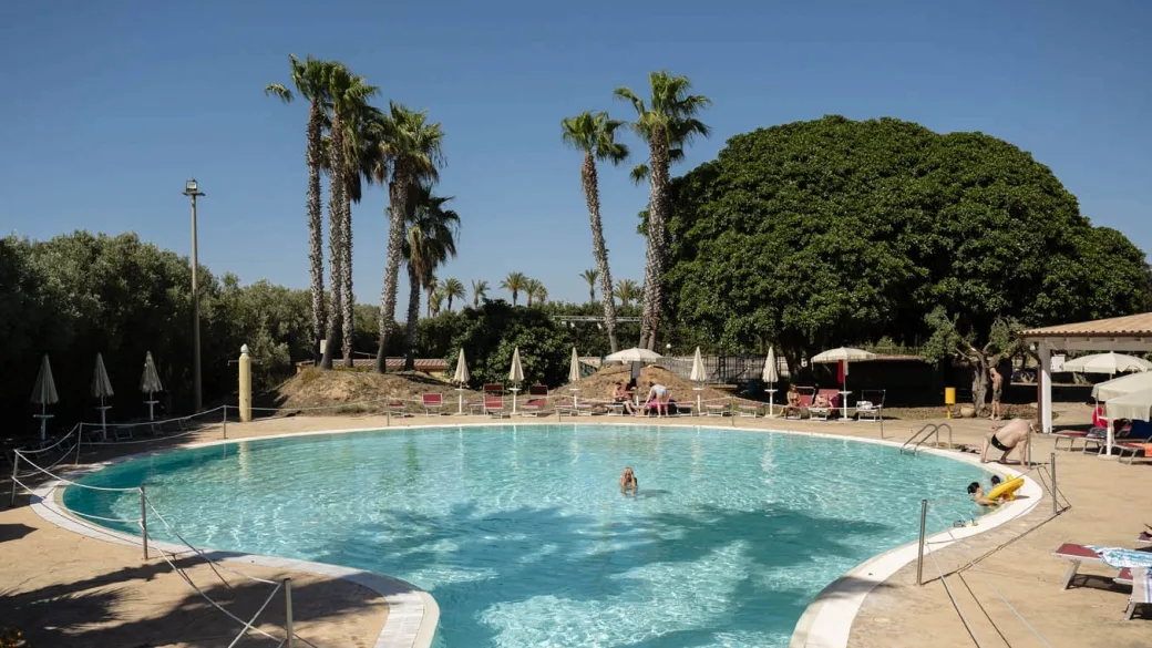 Piscina esterna circolare circondata da palme e lettini con ospiti in acqua