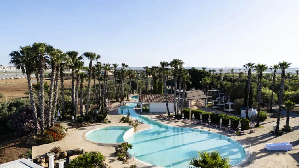 Ampia piscina esterna sinuosa tra palme e vegetazione con vista panoramica