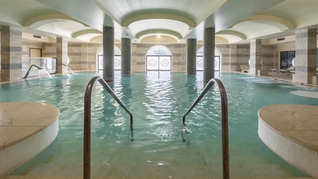 Piscina termale coperta con acqua turchese, colonne e vetrate decorate
