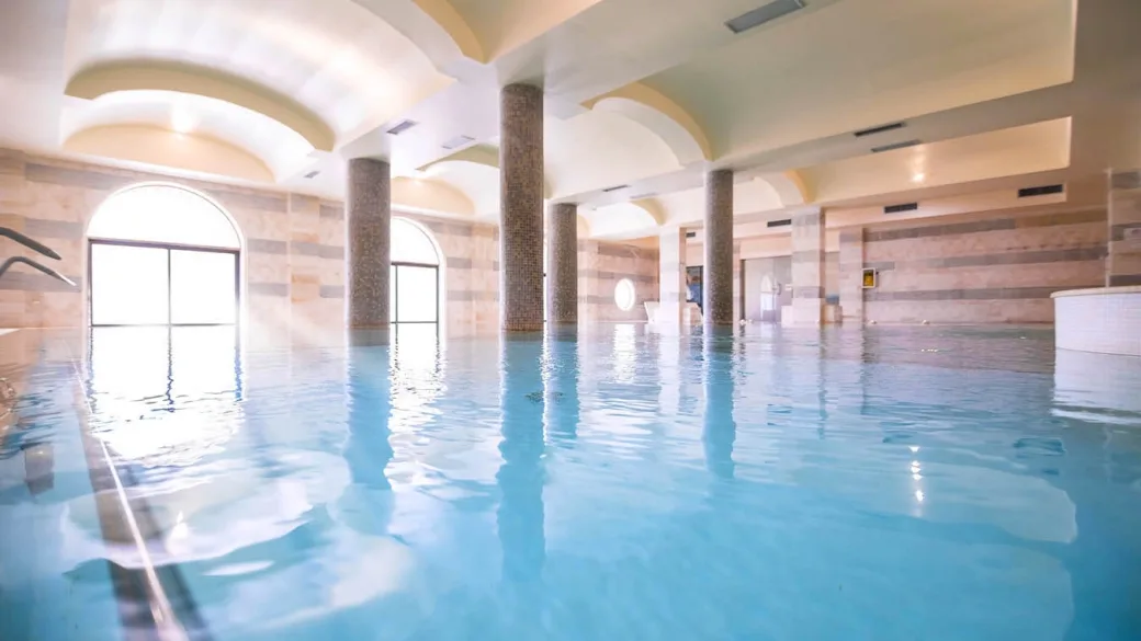 Piscina coperta luminosa con colonne e ampie finestre ad arco