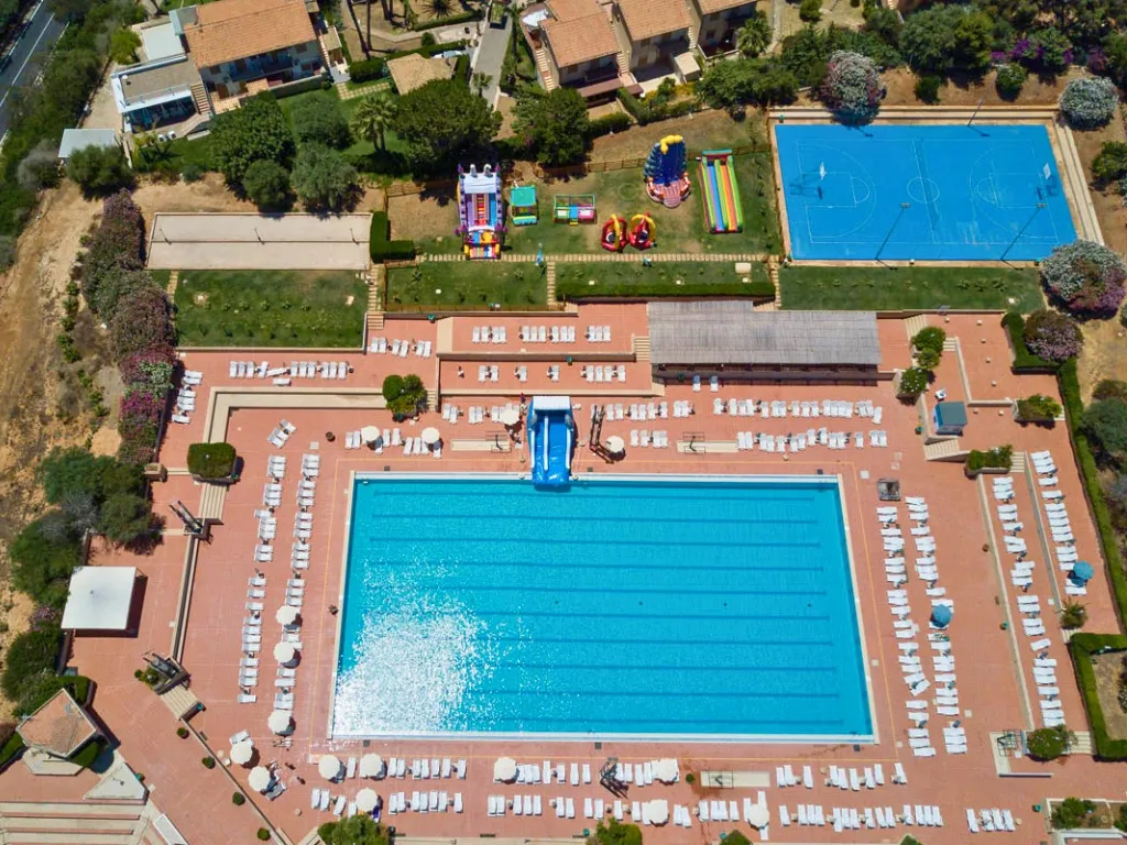 Panoramica aerea della piscina con scivolo, lettini bianchi, gonfiabili e campo da basket