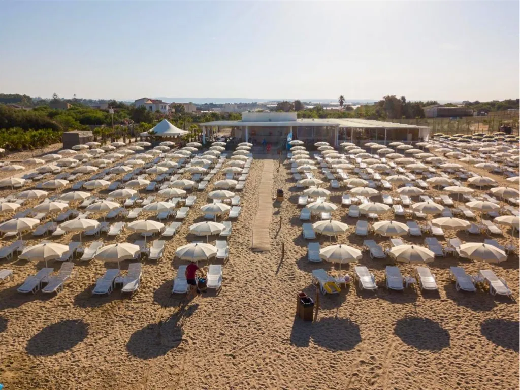 Spiaggia attrezzata con numerosi ombrelloni bianchi e lettini vista dall'alto