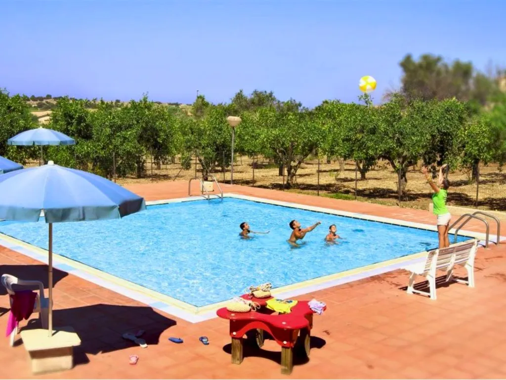 Piscina esterna con persone che giocano in acqua e alberi di agrumi sullo sfondo