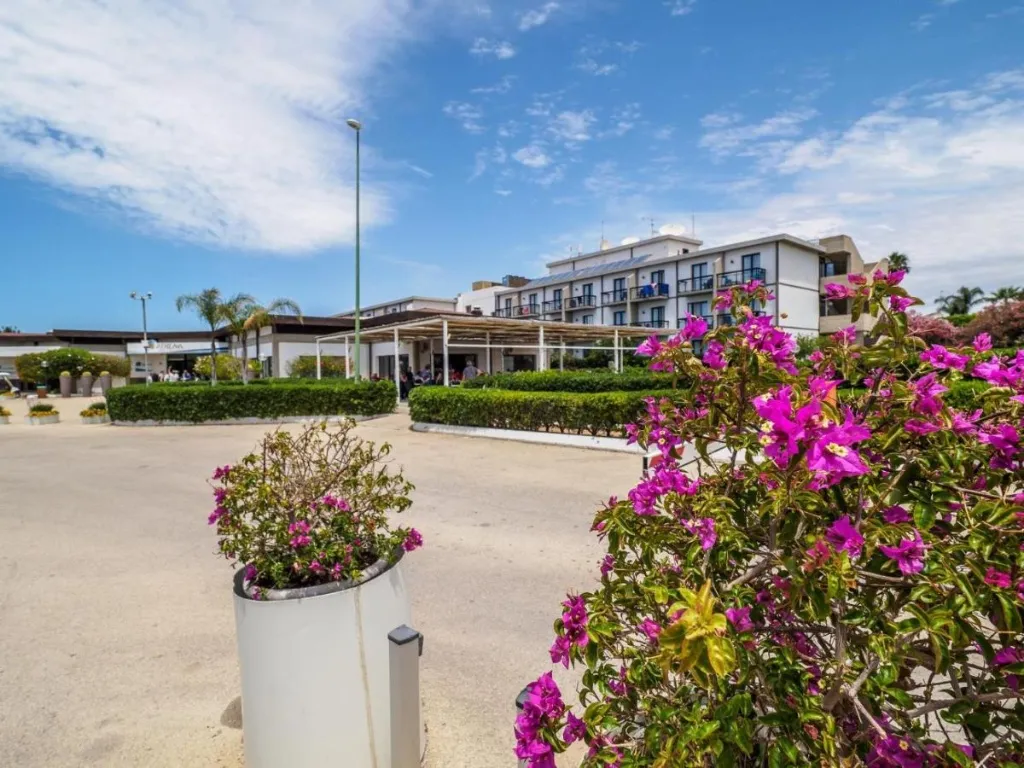 Ingresso dell'hotel con giardino fiorito, bouganville rosa e siepi curate
