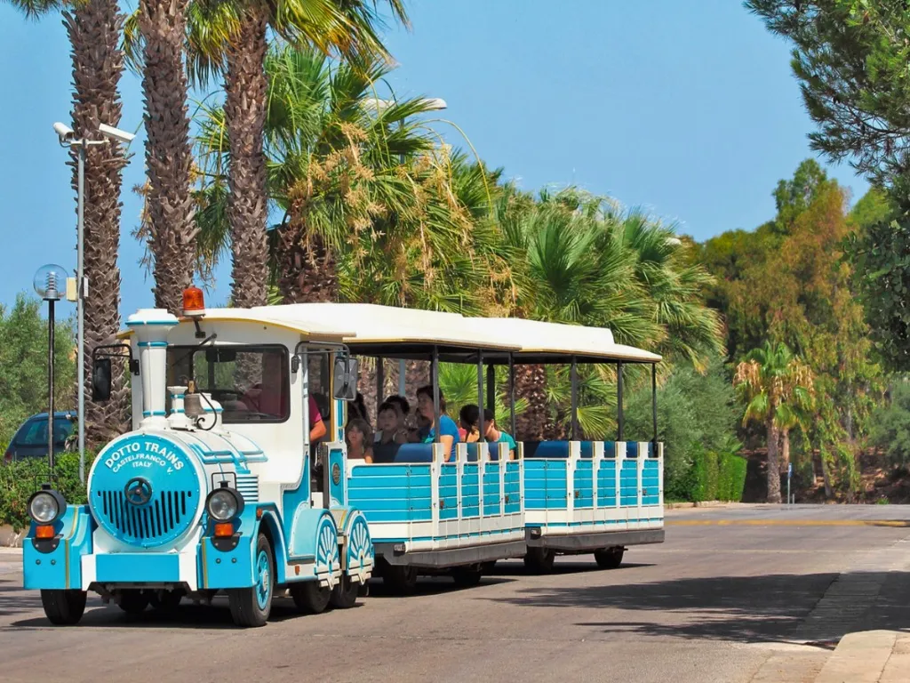 Trenino turistico bianco e azzurro tra le palme del resort