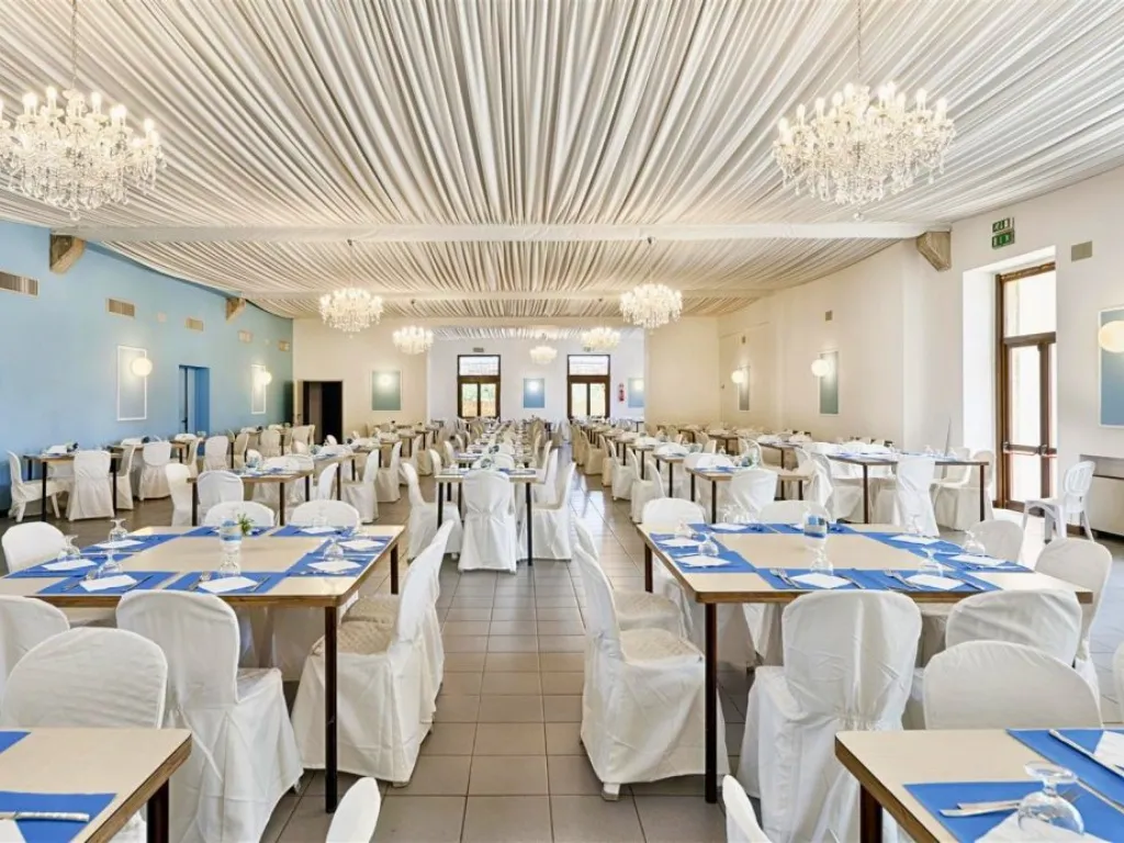 Elegante sala ristorante con lampadari di cristallo, sedie con copertura bianca e tovagliette blu