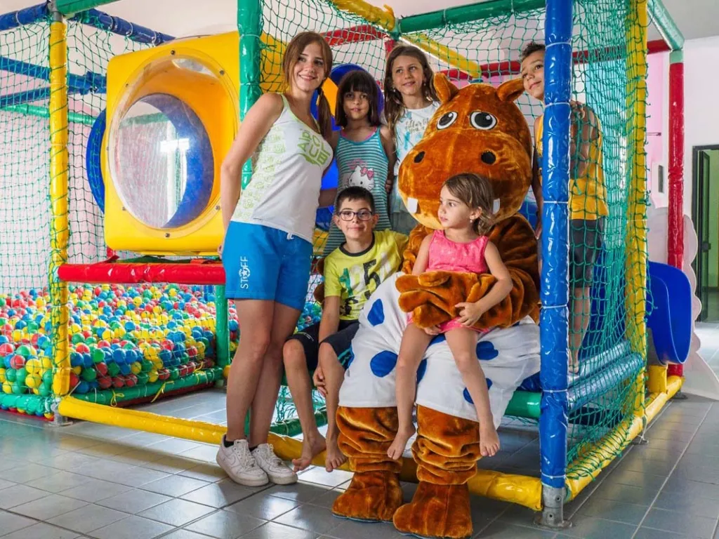 Bambini con animatrice e mascotte ippopotamo nell'area giochi al coperto