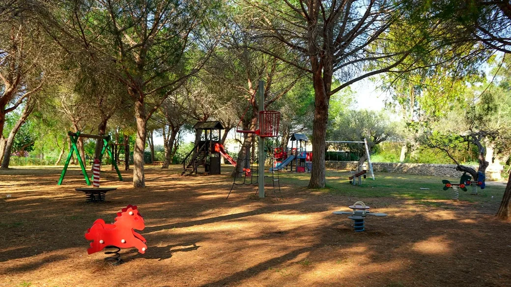 Area giochi per bambini con altalene e giostrine tra alberi ombrosi