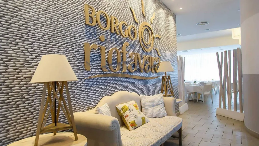 Reception del Borgo Riofavara con parete in pietra, divano beige e lampade decorative