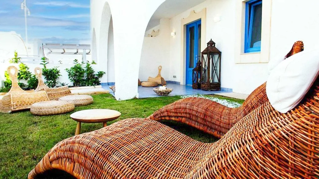 Giardino privato con lettini in vimini intrecciato, tavolino e ingresso con porta blu in stile mediterraneo