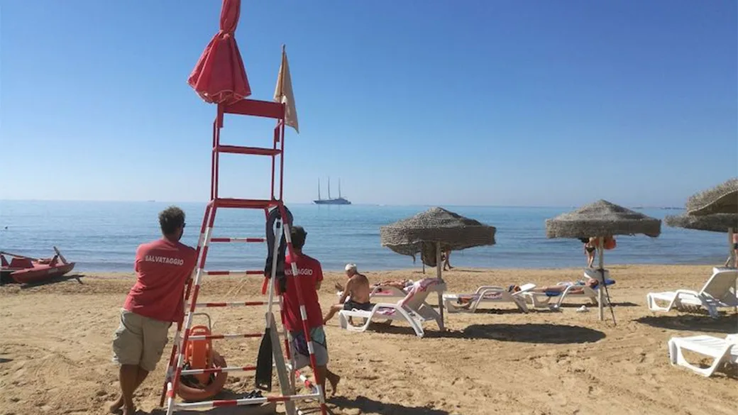 Spiaggia con torretta di salvataggio, bagnini e ombrelloni in paglia