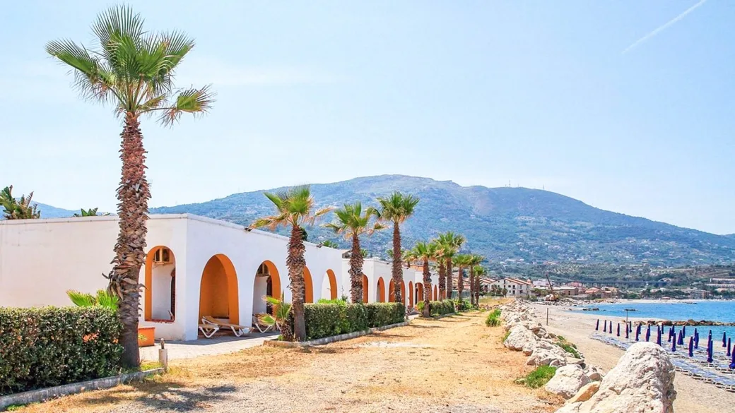 Bungalow bianchi con archi e palme lungo la spiaggia con vista montagne