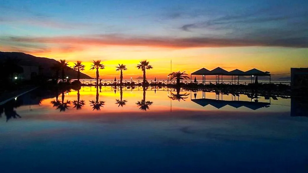 Tramonto colorato riflesso sulla piscina con palme e ombrelloni