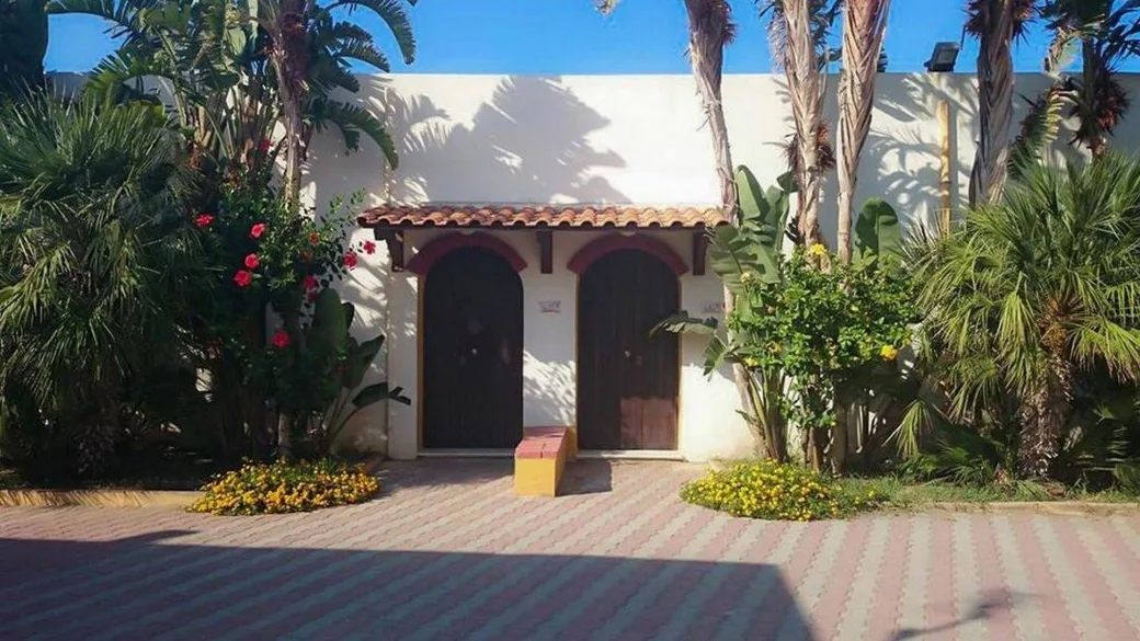 Ingresso di bungalow bianco con porte in legno, palme e fiori