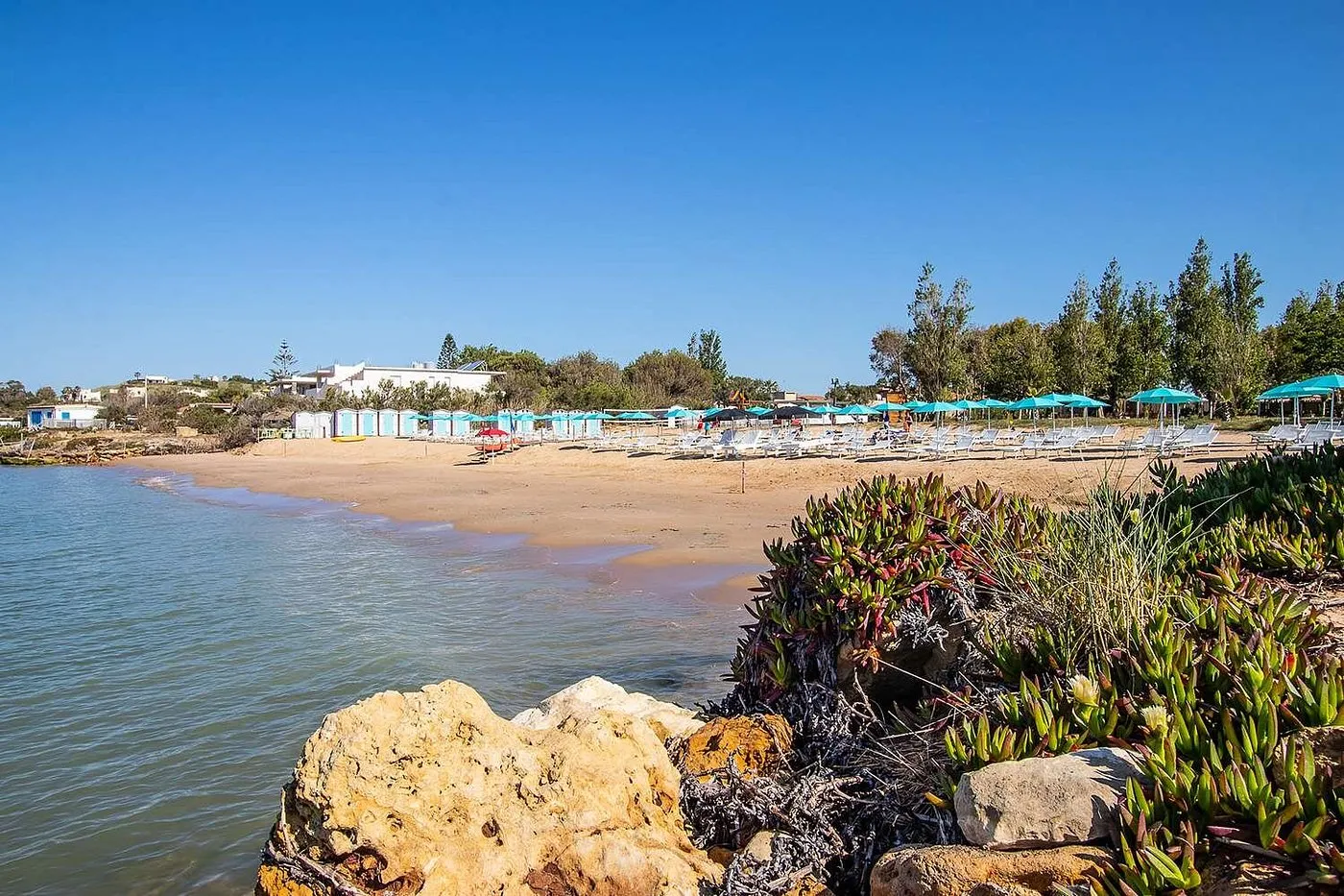 Spiaggia sabbiosa vista dalle rocce con lettini e cabine
