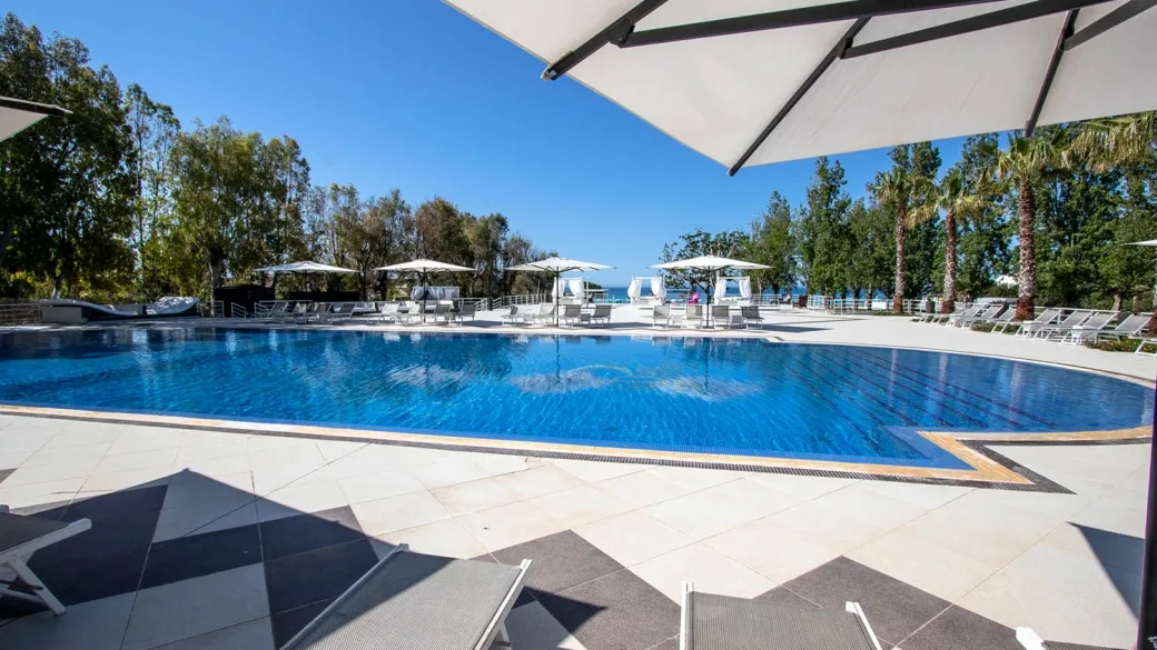 Piscina con ombrelloni bianchi e palme sotto cielo azzurro