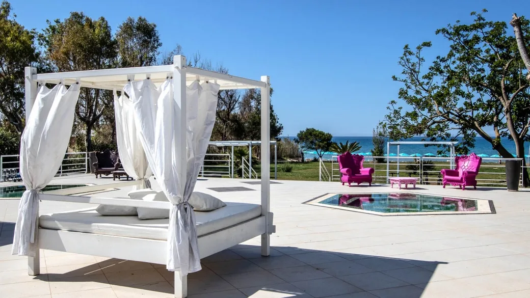 Letto baldacchino bianco su terrazza con vista mare e poltrone fucsia