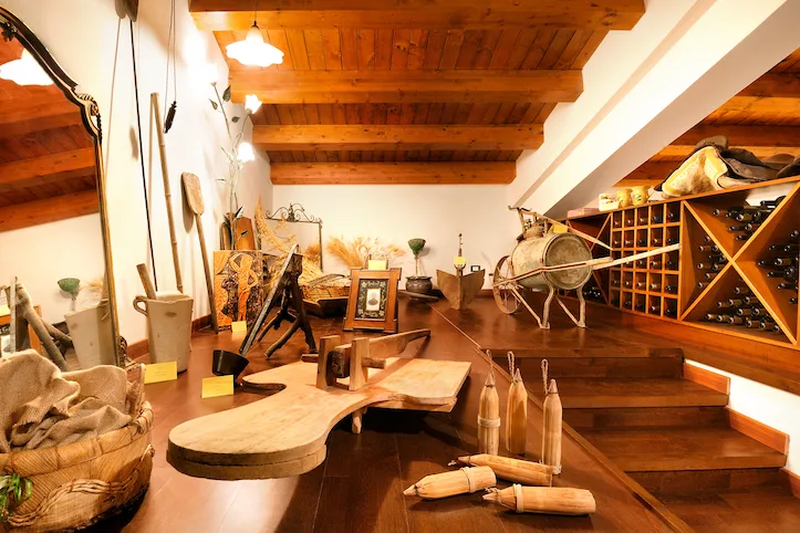 Cantina con soffitto in legno, bottiglie di vino e attrezzi rurali antichi