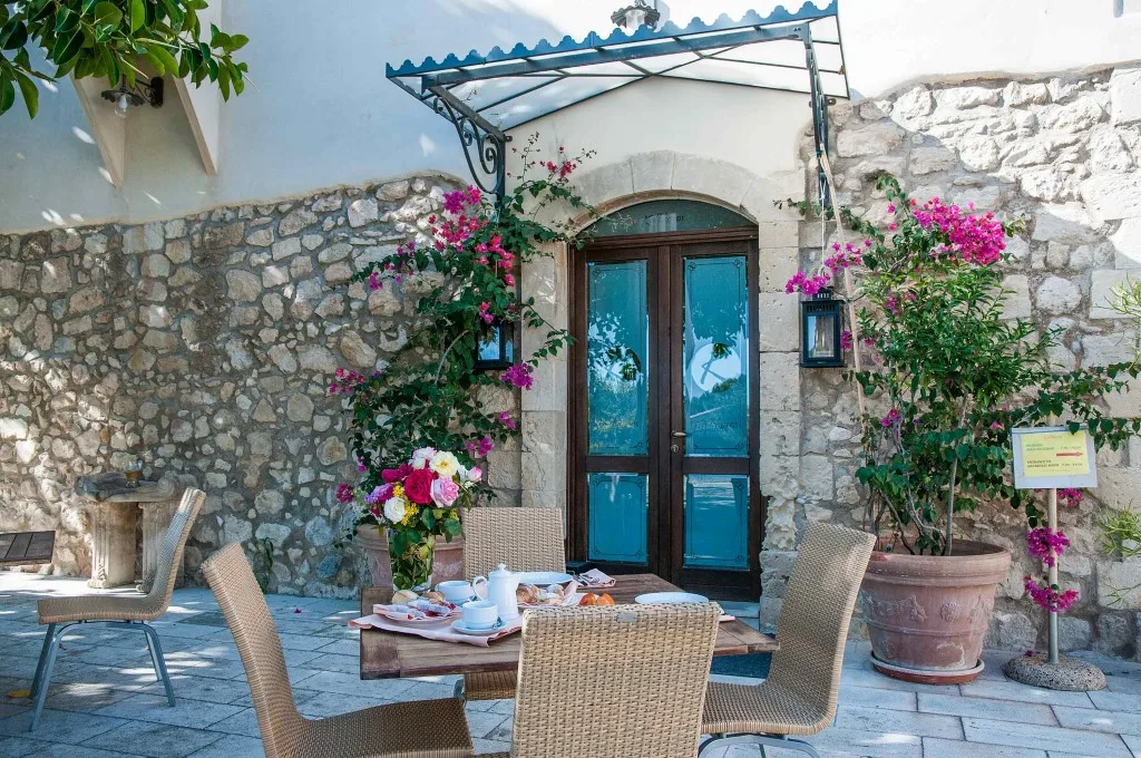 Tavolo per colazione all'aperto in cortile in pietra con fiori e porta blu